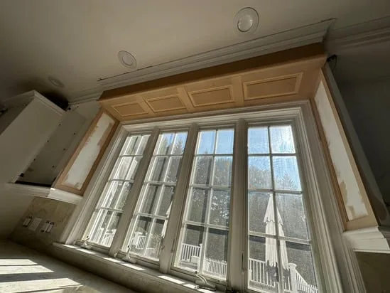 A high-angle photo looking up at a four-panel custom coffered valance installation, showing the detailed woodwork above a wide window bay.