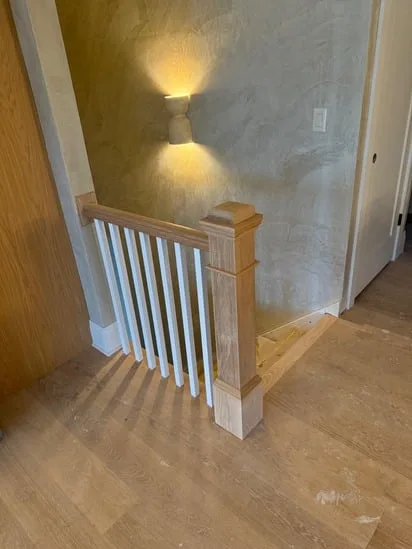 View of the completed finished stair carpentry project, showcasing the installation from a side angle, integrating a custom newel post, balusters, and matching railing elements.