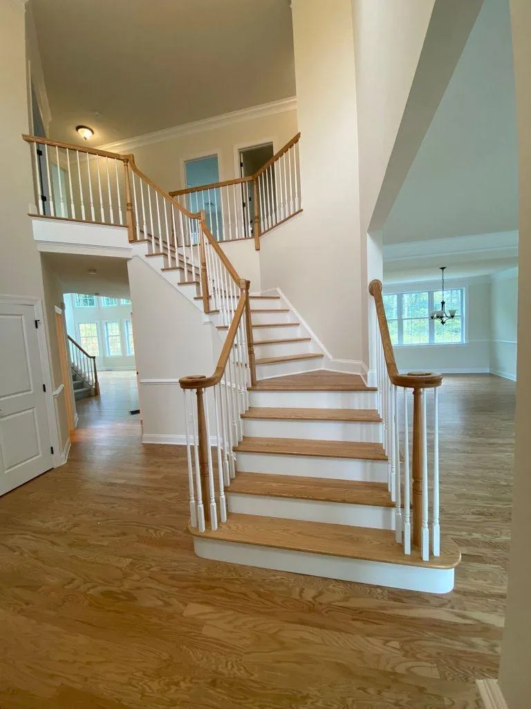 View of a newly installed custom hardwood staircase handrail installation featuring curved oak railings, white spindles, and matching wood treads in a spacious home entryway.
