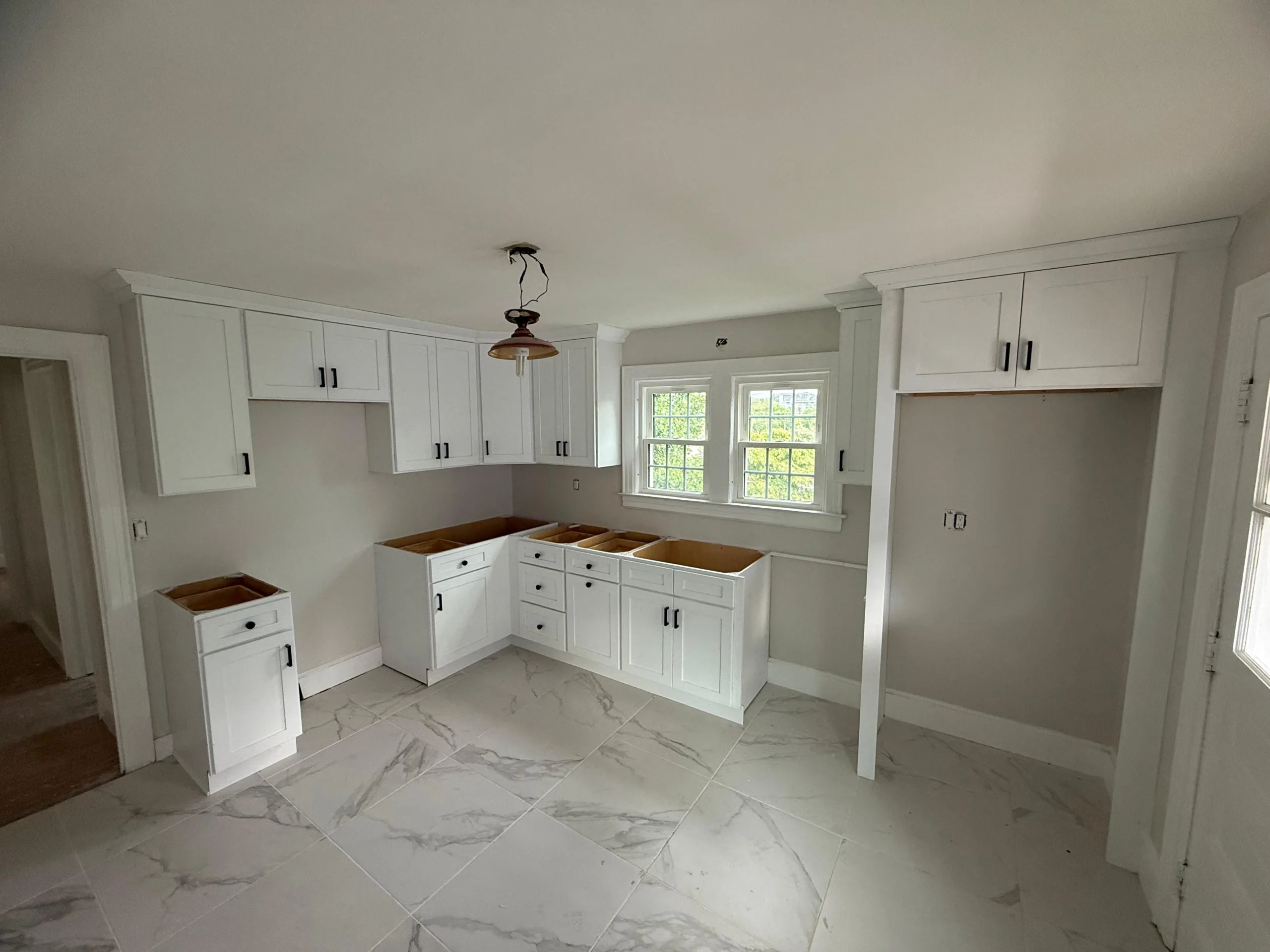 Wide angle view of a custom kitchen cabinet installation including a refrigerator surround and marble-style flooring.