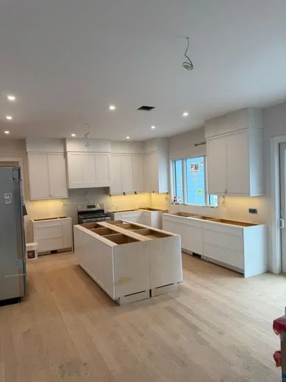 Custom kitchen carpentry work showing the installation of white upper cabinets and a large central island.