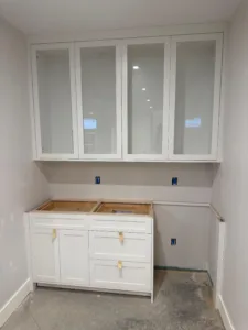 A professional custom laundry cabinetry installation featuring white shaker cabinets and glass-front upper units in a renovated utility room.