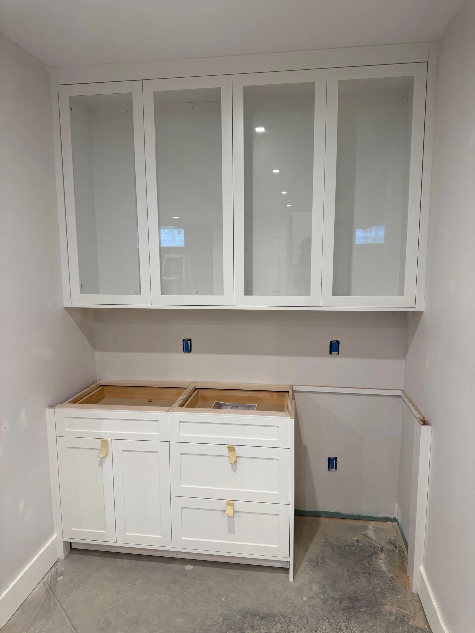 A professional custom laundry cabinetry installation featuring white shaker cabinets and glass-front upper units in a renovated utility room.