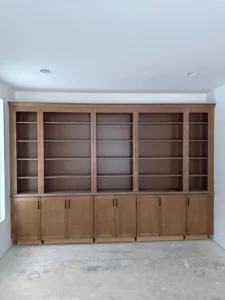 Unfinished custom wooden bookcase with base cabinets and multiple upper shelves.