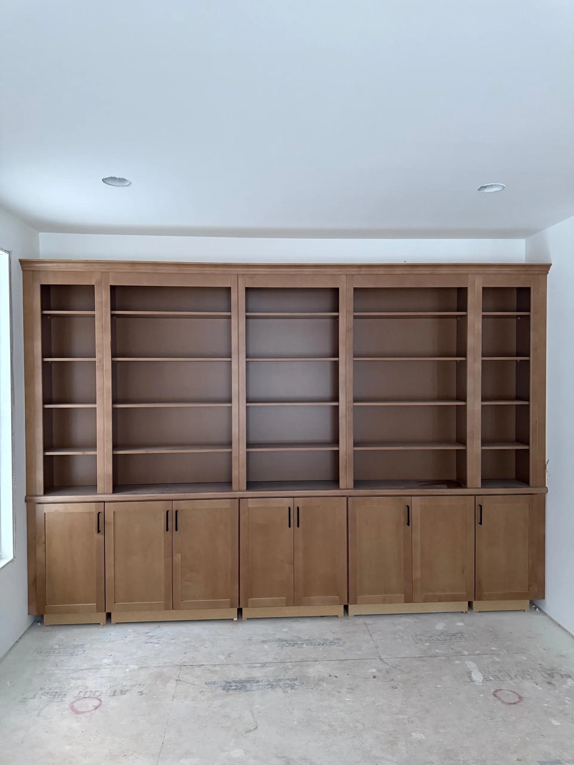 Unfinished custom wooden bookcase with base cabinets and multiple upper shelves.
