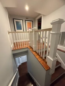 Looking down at a lower level during a custom staircase carpentry project, showing the structural framework of newel posts and handrails above wooden stairs.