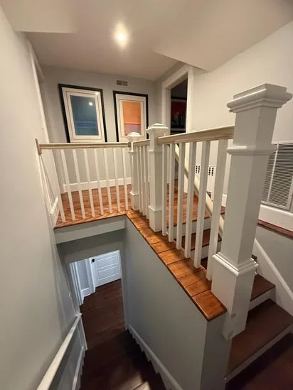 Looking down at a lower level during a custom staircase carpentry project, showing the structural framework of newel posts and handrails above wooden stairs.