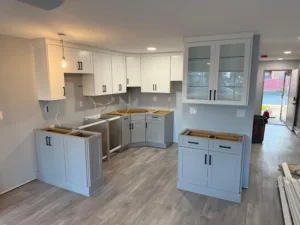 Perspective view of a completed two-tone cabinet installation with glass-front uppers and a kitchen peninsula.