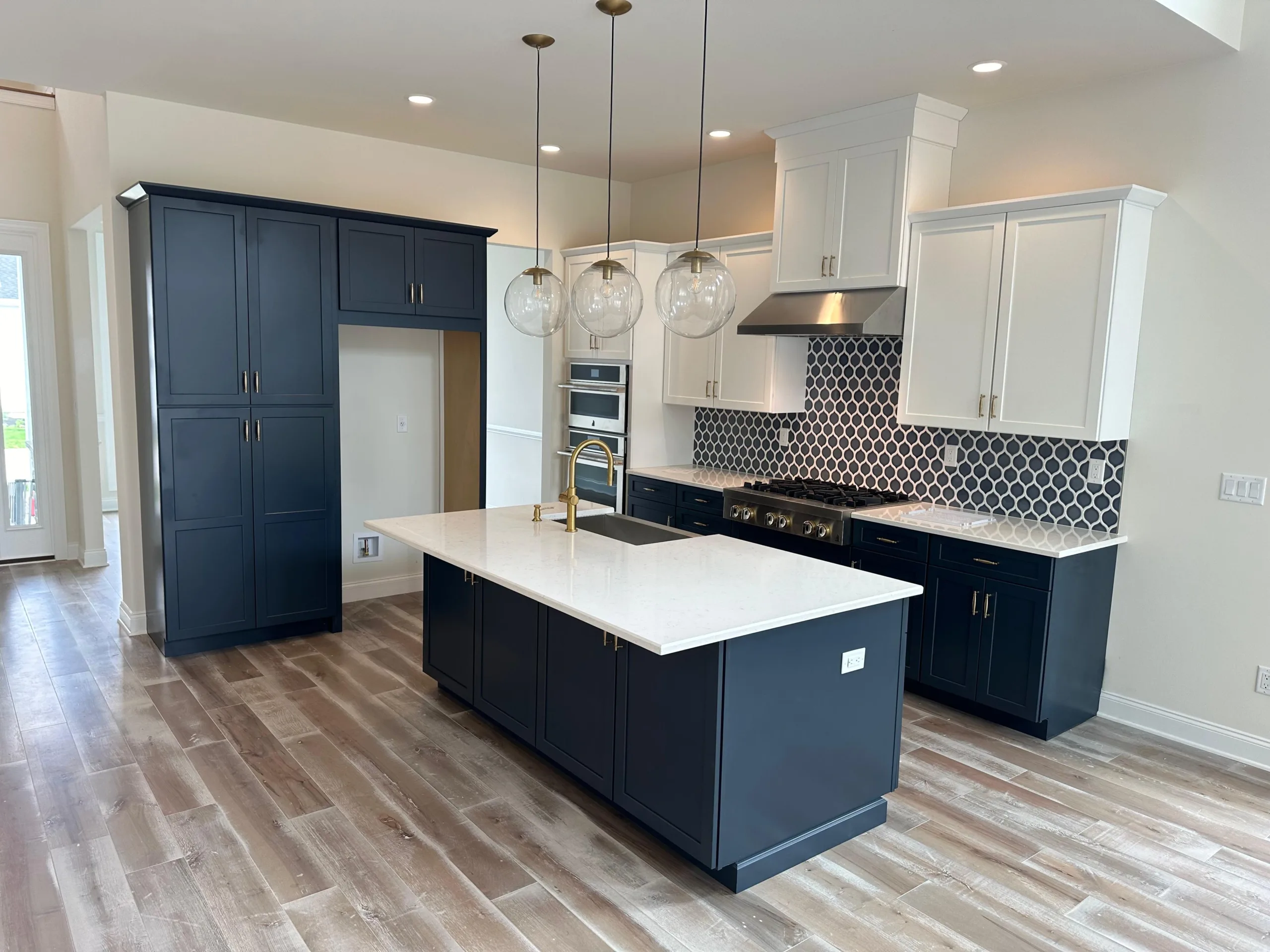 Modern kitchen featuring custom navy kitchen cabinets, a large central island with white quartz countertops, and decorative globe pendant lighting.