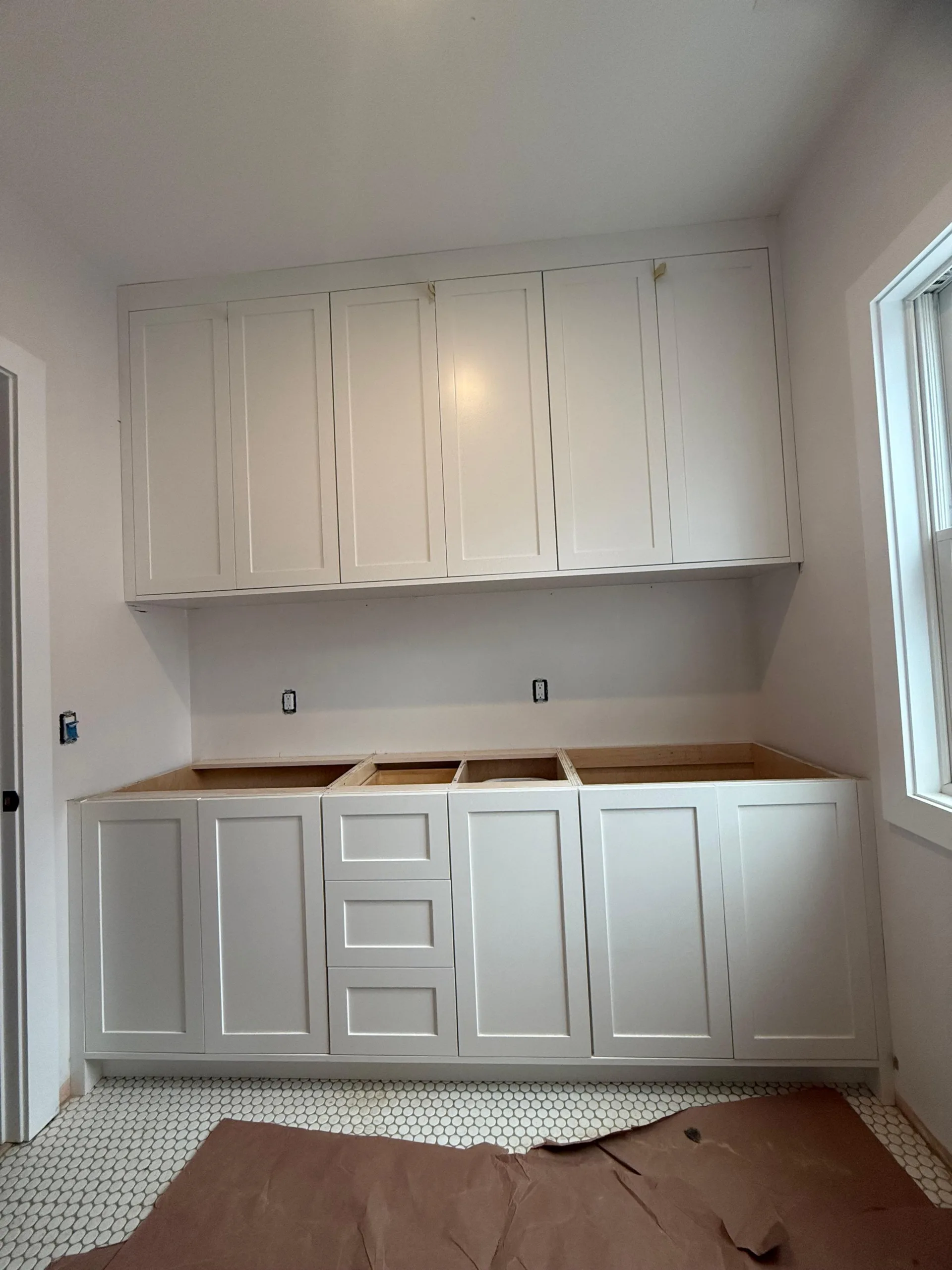 A detailed view of white shaker custom cabinets installed in a bright room with penny tile flooring.
