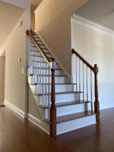 A side-angle view of a professionally completed staircase renovation featuring dark wood treads and handrail with white risers and balusters.