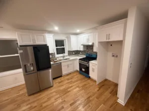 Modern kitchen remodel featuring custom white kitchen cabinets, stainless steel appliances, and hardwood floors.