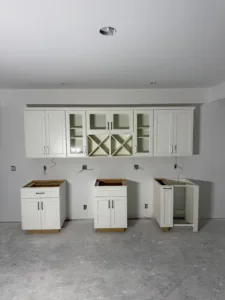 A professional installation of custom white shaker cabinetry featuring upper glass doors and integrated wine racks against a white wall.