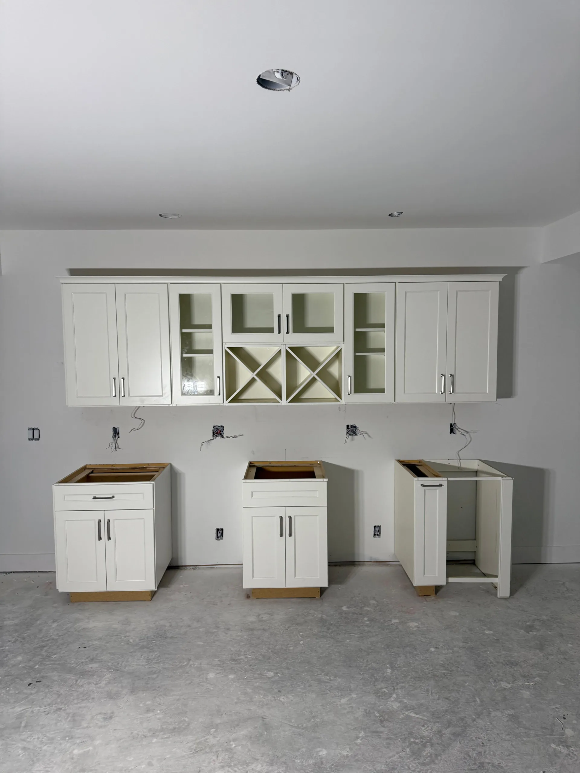 A professional installation of custom white shaker cabinetry featuring upper glass doors and integrated wine racks against a white wall.